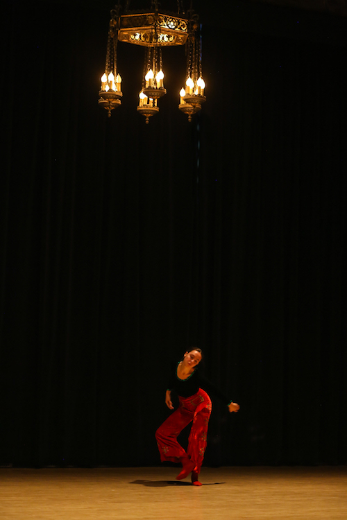 Erdman in red velvet pants dances under a chandelier
